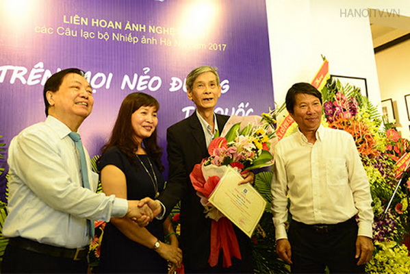 Nghệ sĩ Nhiếp ảnh Nguyễn Tất Lộc (ôm hoa) tại triển lãm cá nhân của mình.